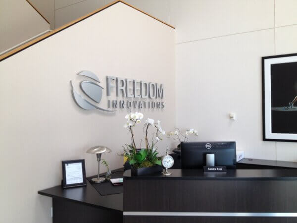 Photo of a corner of a lobby - behind a black desk is a mounted sign that reads "Freedom Innovations"