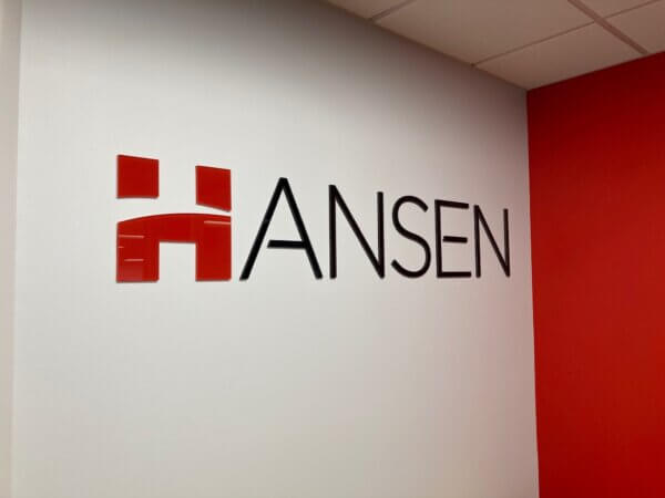 Photo shows a simple lobby sign  - the sign reads "Hansen" and the H is a fancy red font while the rest of the word is a simple black font