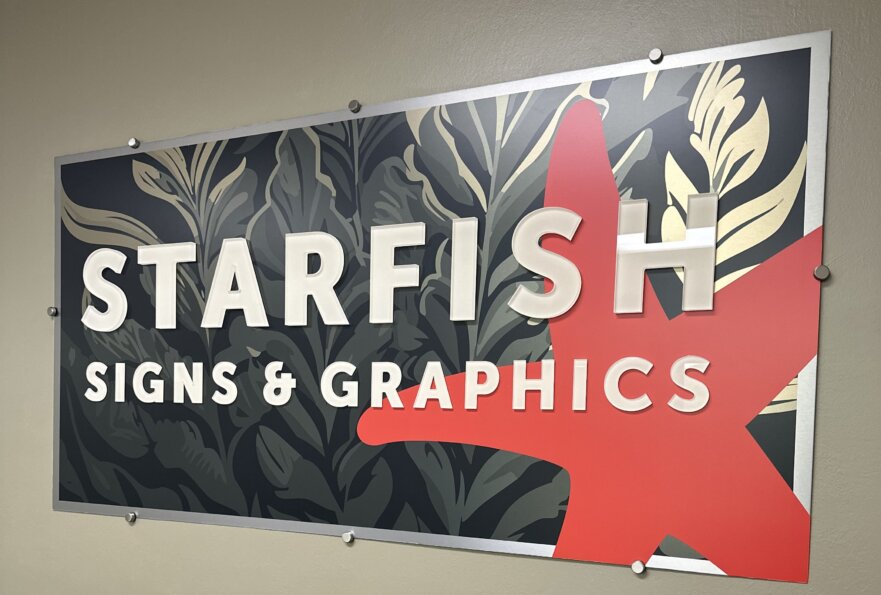 photograph of lobby sign - a mounted sign features the Starfish company name, with a red starfish on the right, all set atop a background of a kelp bed