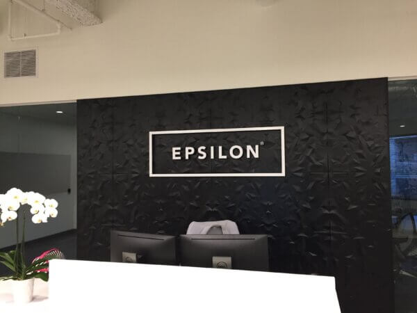 Photo of a black lobby wall, with a white lobby sign - the word 'Epsilon' is mounted in a white boxed outline