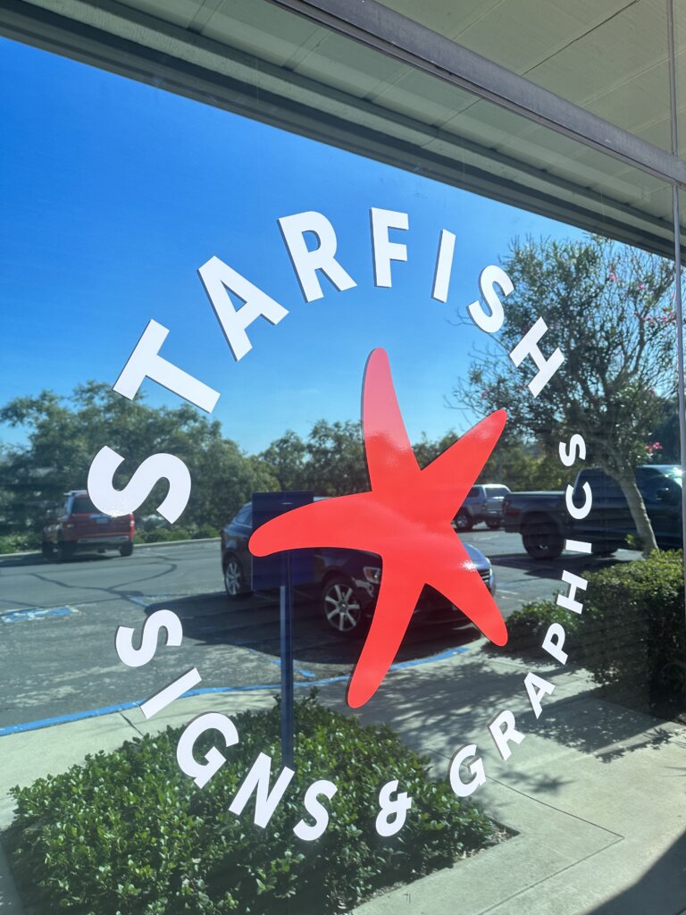 photograph of window signage - a red starfish is circled by white letters that read "Starfish Signs & Graphics"