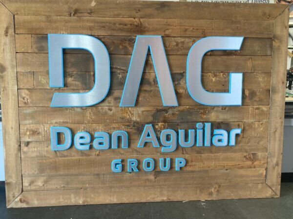 Photo of wooden office sign, inlaid with aluminum lettering that reads "DAG: Dean Aguilar Group".